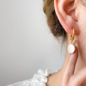 Boucles d'oreilles dorées avec zircon carré et pendentif en nacre portées par un mannequin