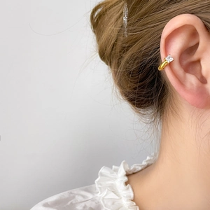 Gros plan détaillé d'un ear cuff doré avec zircon carré porté par un mannequin