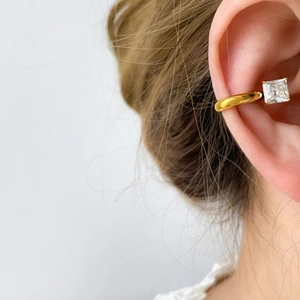 Vue macro d'une bague d'oreille dorée avec zircone carrée portée sur un modèle