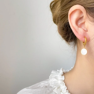 Gros plan de boucles d'oreilles créoles dorées avec pendentif en nacre sur modèle