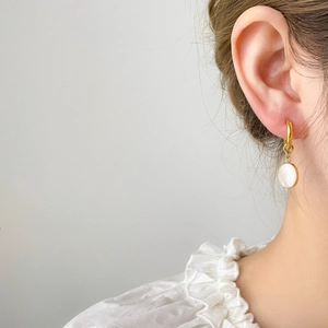 Gros plan de boucles d'oreilles dorées avec pendentifs en nacre portées par un modèle