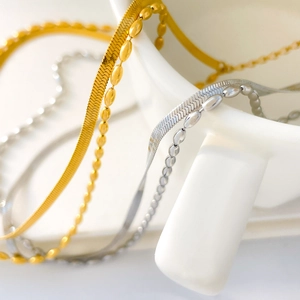 Detail of silver and gold herringbone and satellite layered chains on ceramic