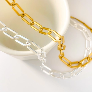 Close-up of gold and silver rectangle link chains draped over white ceramic bowl