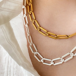 Dual gold and silver paperclip chain necklaces layered over a white linen shirt