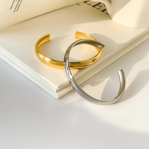 Polished gold and silver C-shaped cuff bracelets stacked on a minimalist white book