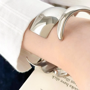 Detailed macro shot of a wide polished silver cuff bracelet worn over a white knit sleeve