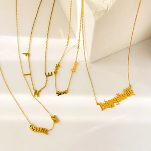 Colliers en acier titane plaqué or 18K avec pendentifs lettres sur socle blanc minimaliste