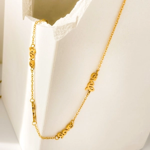 Détail macro d'un collier en acier titane doré avec pendentifs 'love' sur pierre blanche