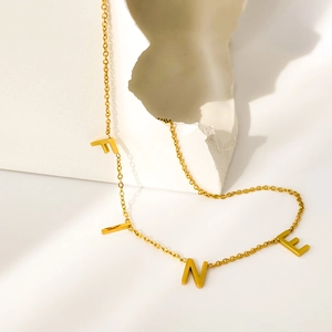 Gros plan du collier en titane doré avec pendentifs lettres FINE sur fond de pierre