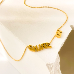 Détail du collier avec pendentif lettre SHINE ON doré sur fond de pierre blanche épuré