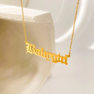 Gros plan d'un collier pendentif Babygirl plaqué or 18 carats sur un support en pierre blanche