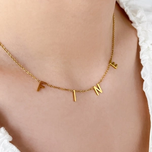 Détail du collier en acier titane doré avec des lettres coulissantes épelant le mot FINE