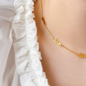 Gros plan du collier en titane doré avec pendentifs 'love' sur le décolleté d'un mannequin