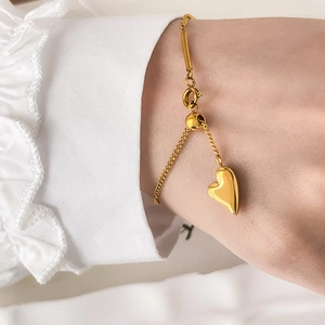 Bracelet à pendentif cœur doré réglable porté au poignet sur fond de volants élégants