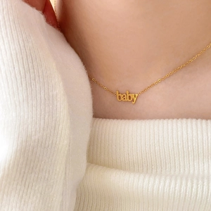 Dettaglio di una collana dorata con ciondolo a lettera baby indossata da una modella