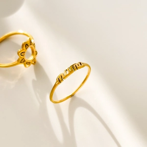 Macro detail of 18K gold plated sunflower ring and MAMA letter ring with soft shadows