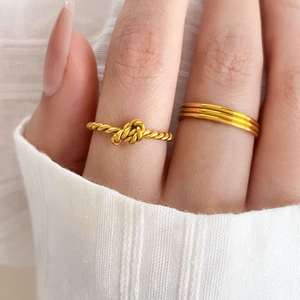 Detail of twisted rope knot ring and triple-layer gold ring set on model's hand