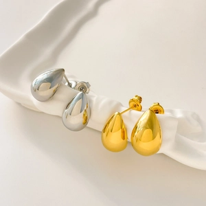 Macro shot of polished gold and silver water drop earrings on a ceramic tray