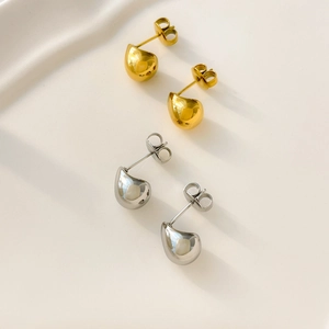 Polished hollow drop earrings in gold and silver steel finishes on a white texture background