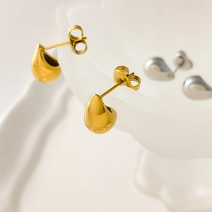 Macro view of polished gold and silver teardrop stud earrings on wavy tray
