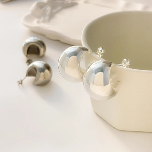 Close-up of minimalist polished silver C-shaped dome stud earrings on ceramic cup
