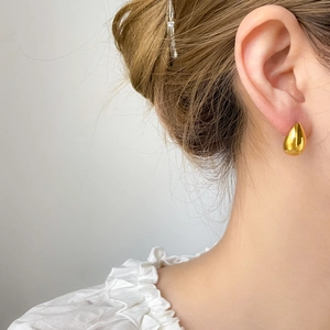 Macro detail of polished gold teardrop stud earring worn by a model in soft lighting