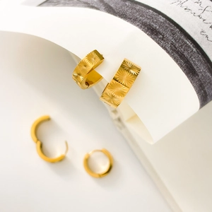Dettaglio macro di orecchini a cerchio in oro 18K con incisione a stella e finitura lucida