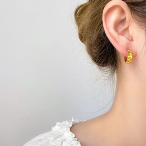 Dettaglio di orecchini in titanio placcati oro 18K con motivo a raggiera sulla modella