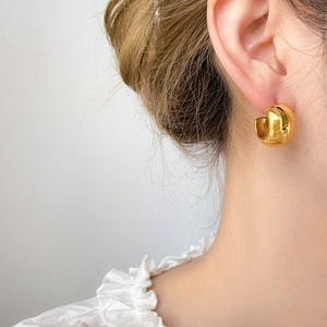 Macro side view of thick C-shaped gold-plated hoop earring on a female model