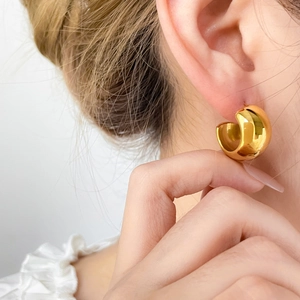 Close-up of a person wearing chunky C-shaped gold-plated stainless steel hoop earrings