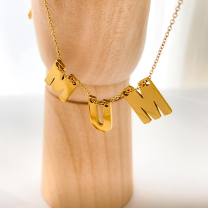 Détail du collier avec pendentif MUM plaqué or 18 carats sur un support en bois