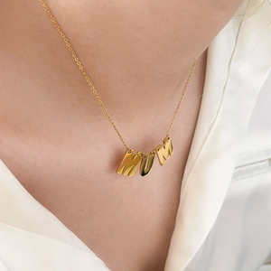 Détail du collier avec lettres MUM dorées porté par un mannequin sur soie blanche