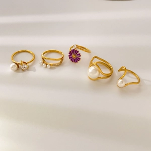 Set of gold rings with pearls, pear-shaped zircons and purple enamel flowers on white