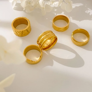 Detail showing five assorted gold-plated titanium steel rings with textured patterns
