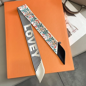 Detailed view of floral silk twilly scarf with Foxey logo on an orange gift box