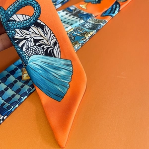 Close-up of luxury orange silk scarf with blue artistic patterns and diagonal twill texture