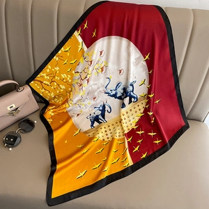 Detailed view of square silk scarf with elephant prints on a beige leather sofa