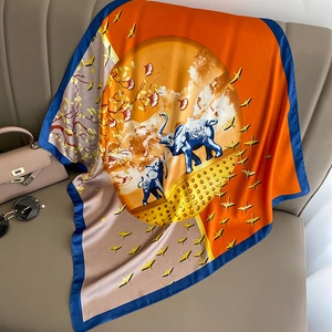 Artistic orange silk-like scarf with elephant print draped on a brown leather sofa