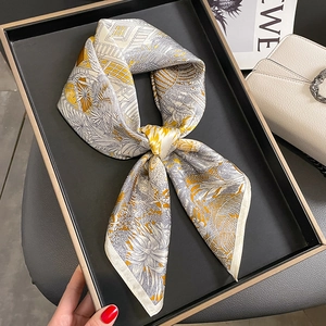 Elegant silk square scarf with yellow and gray geometric plant patterns on a display tray