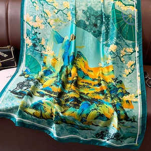 Classic Chinese landscape silk scarf with teal and gold floral scenery on leather sofa