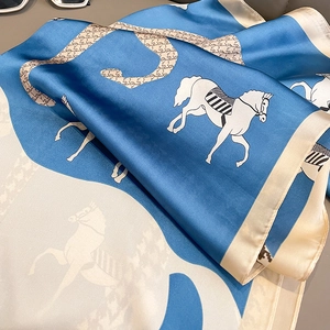 Detail of silk-like scarf featuring horse prints and houndstooth patterns in blue and beige