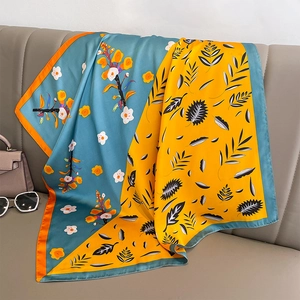 Carré de soie aux motifs floraux bleu et jaune drapé élégamment sur un canapé gris