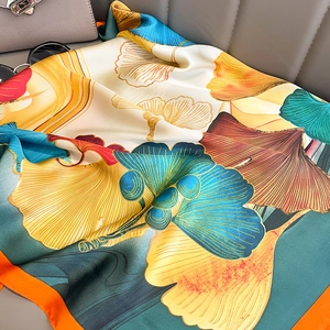 Écharpe élégante en soie avec motif de feuilles de ginkgo et bordure orange sur canapé