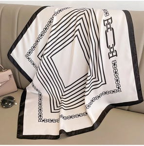 Dettaglio di foulard in seta bianco e nero con motivi a catena su divano in pelle beige