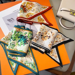 Vue détaillée de trois foulards en soie à fleurs sur une boîte cadeau orange de luxe