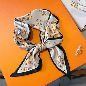 Vue détaillée d'un foulard étroit en soie à motif floral noué sur un sac à main élégant