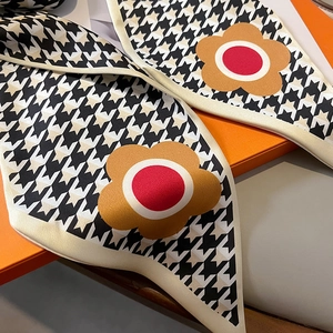 Macro detail of houndstooth silk twilly scarf with floral accents on an orange gift box