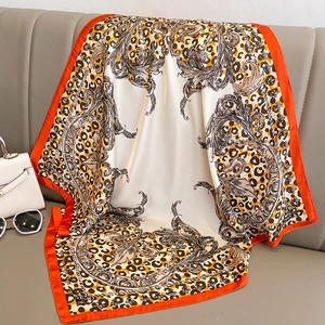 Detail of silk square scarf with leopard print and orange border on leather surface