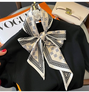 Detail of paisley silk scarf tied in a bow with a camellia brooch on black knitwear