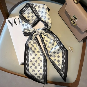 Elegant skinny silk scarf with black geometric patterns tied in a bow on a luxury leather bag